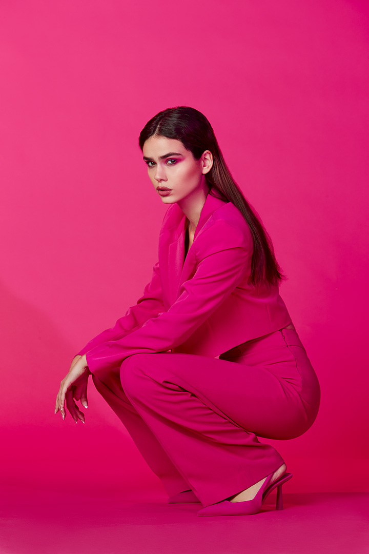 Crouching model in a pink tailored suit against a matching pink backdrop