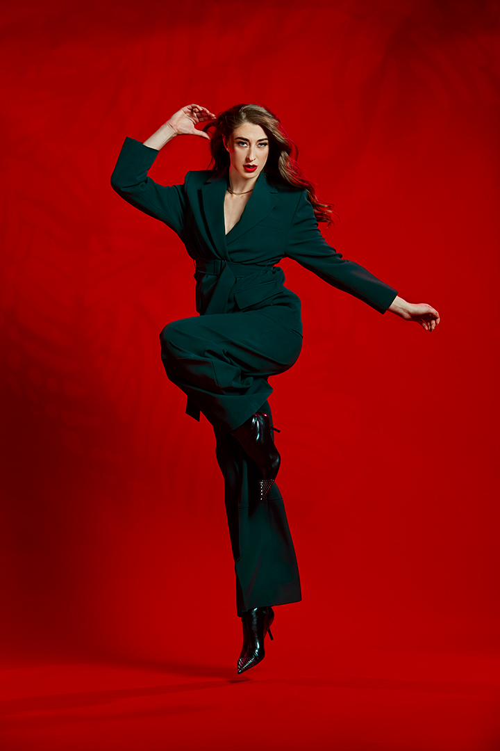 Model in a green suit striking a pose against a red backdrop, fashion editorial