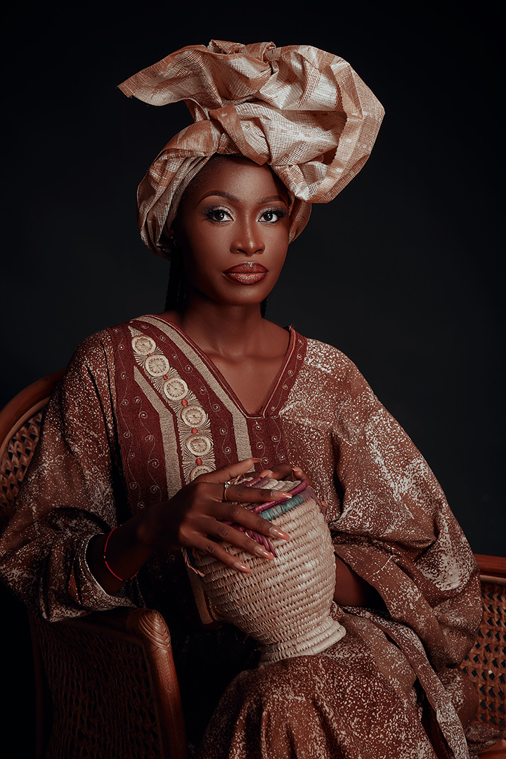Editorial portrait of a woman in a head wrap and embroidered robe against a dark backdrop