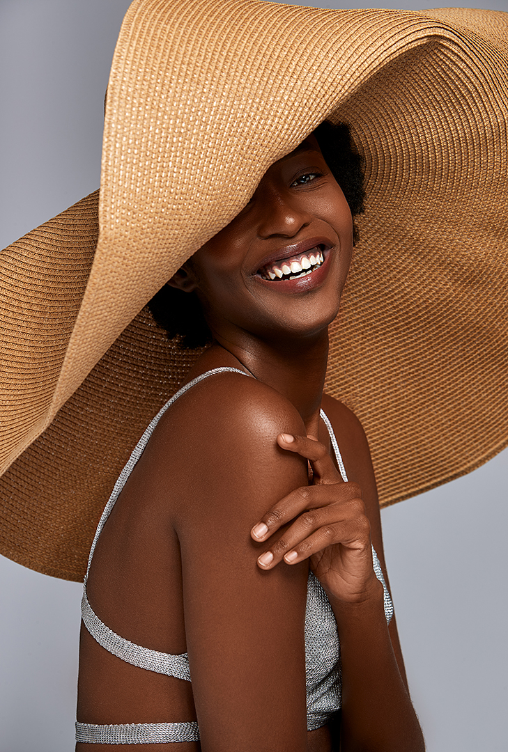 Beauty portrait of a smiling model beneath an oversized straw hat