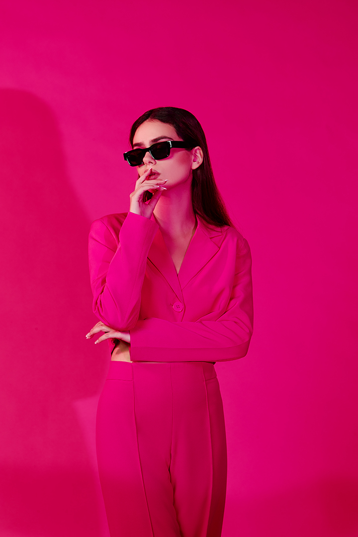 Model in a hot pink suit and black sunglasses against a pink backdrop, fashion editorial