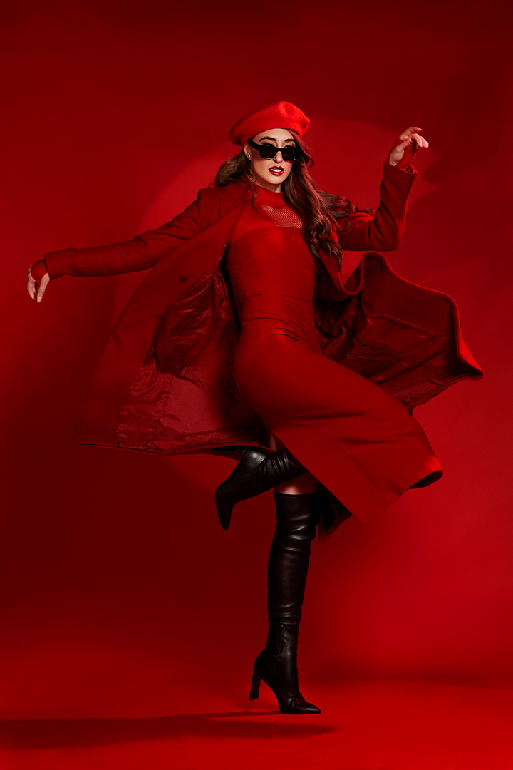 Fashion campaign photo of a model in a red coat and beret mid-step on an all-red set