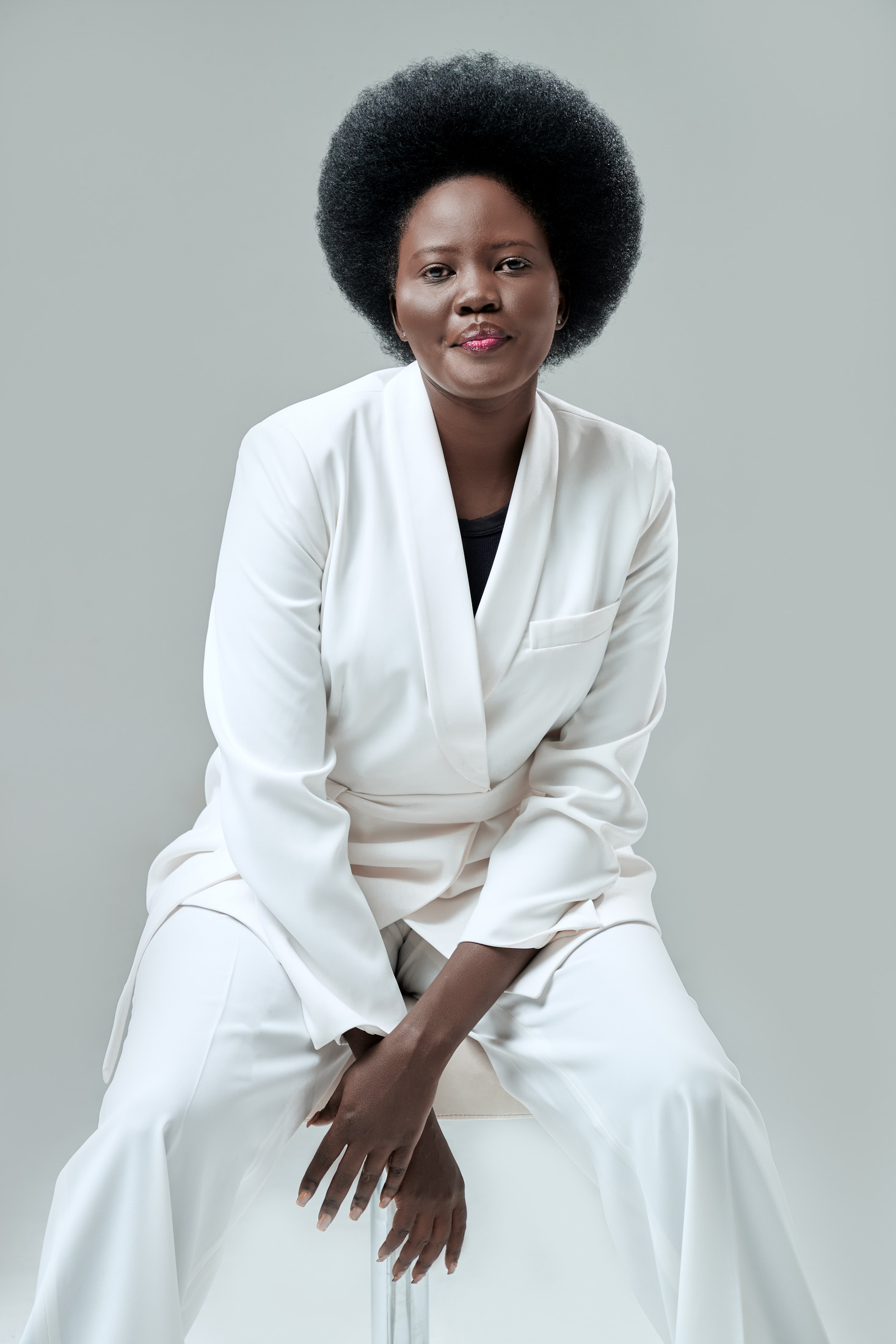 Seated fashion portrait of a woman in a white suit on a soft grey backdrop