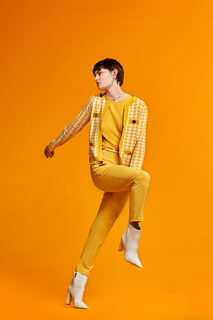Model in a yellow knit jacket and trousers against an orange backdrop, fashion shoot