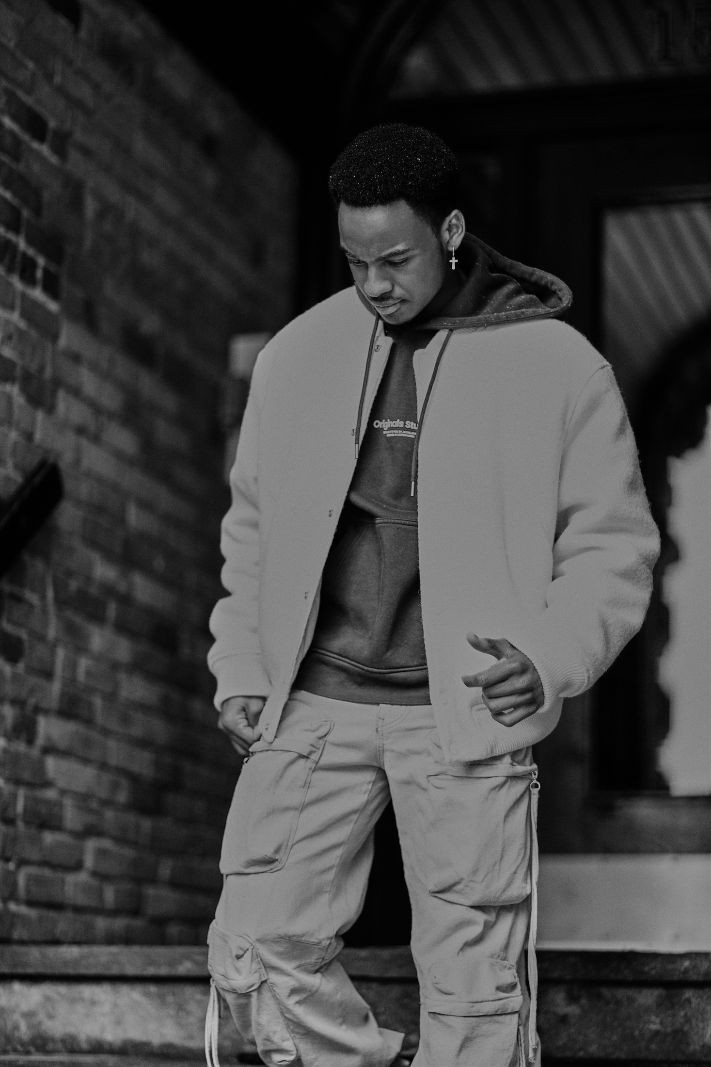 Black and white portrait of a man in a jacket beside a brick wall, streetwear style