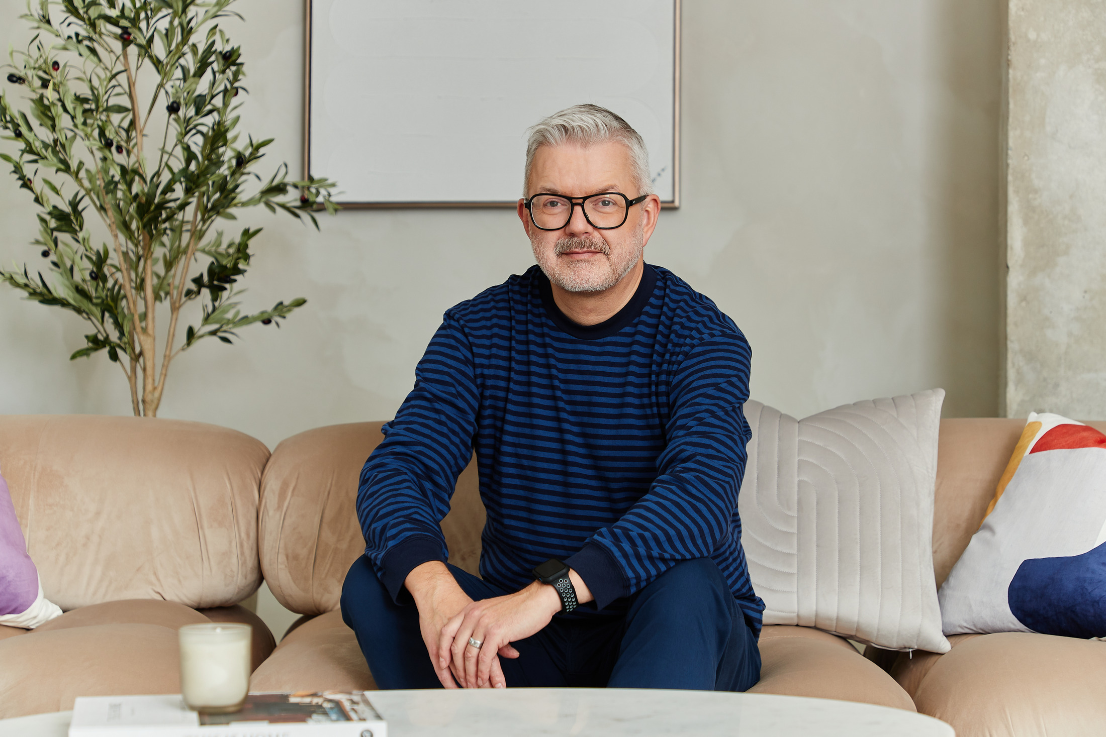 Portrait of a man in a navy striped sweater seated on a beige sofa, looking into the camera